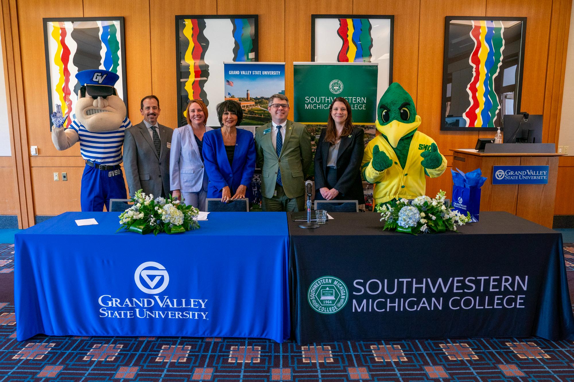 GVSU representative and SMC representatives standing behind tables and respective college banners